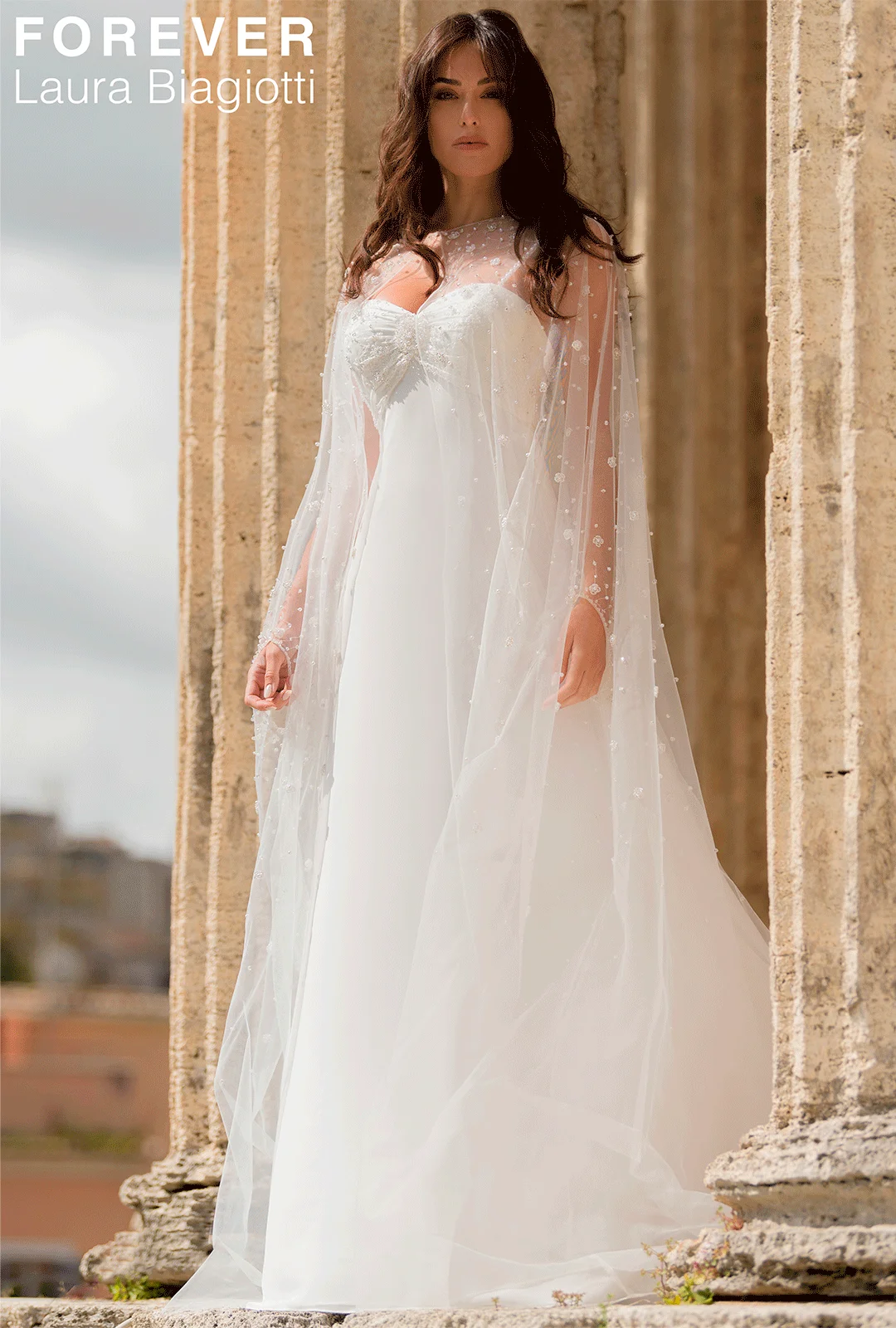 Abito da sposa Laura Biagiotti Roma con mantello di tulle ricamato. Design elegante e romantico per il giorno del sì.
