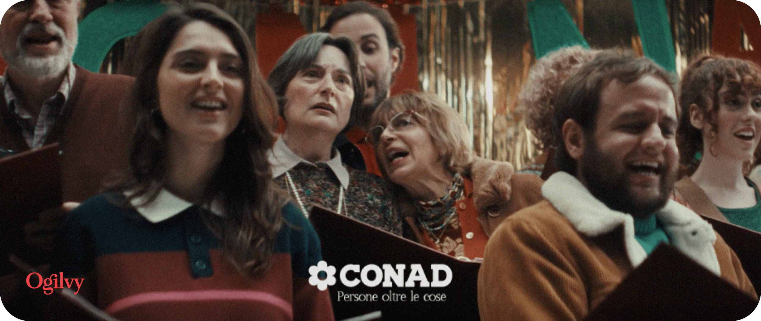 Coro natalizio CONAD, agenzia marketing GDO Italia. Persone cantano con gioia, banner promozionale.
