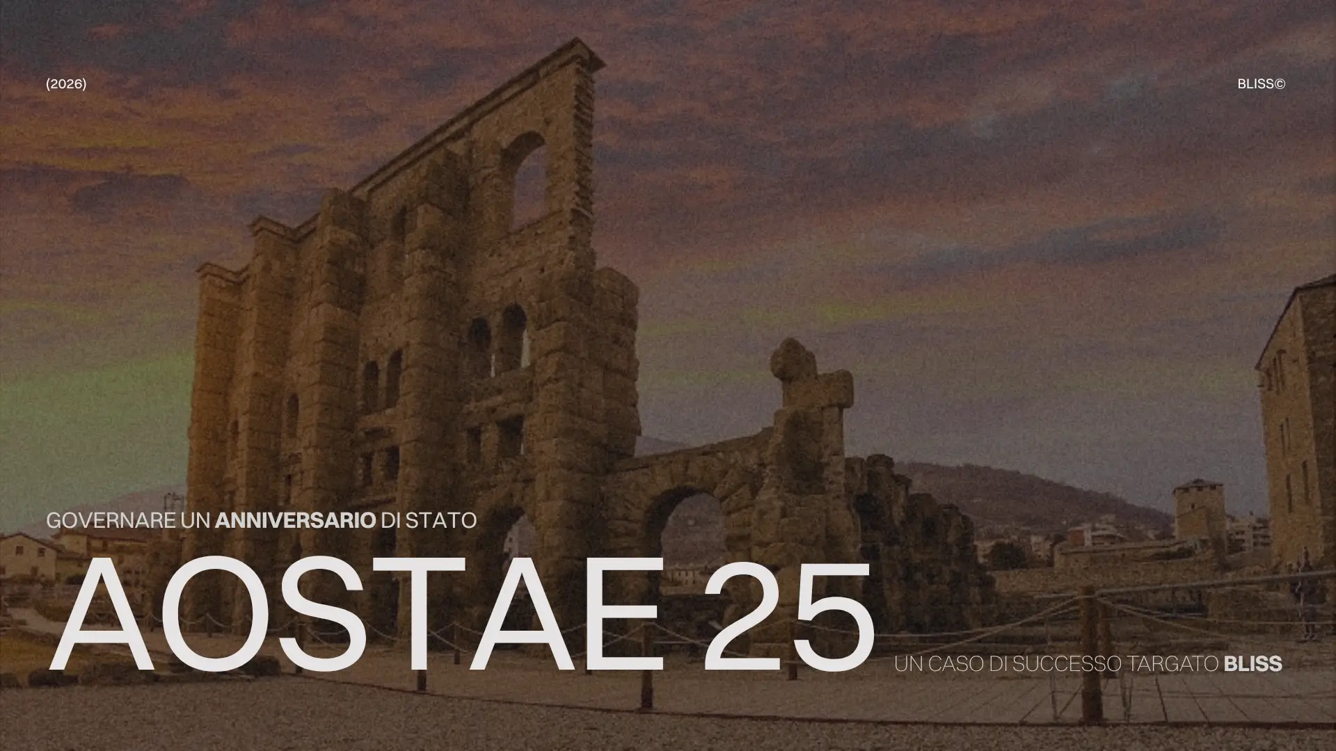 L'Arena romana di Aosta illuminata al tramonto, con il testo "GOVERNARE UN ANNIVERSARIO DI STATO AOSTAE 25".