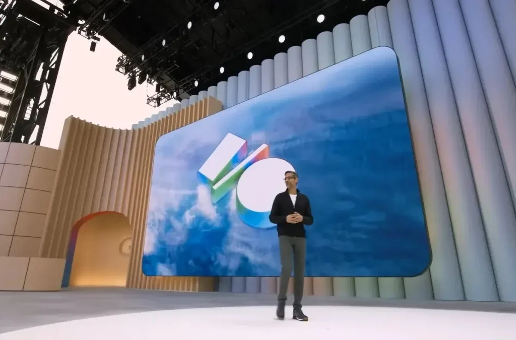 Man in a dark suit presenting in front of a screen with a multicoloured abstract logo, on an illuminated stage.