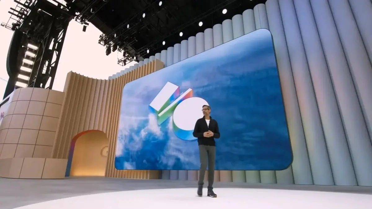 Uomo in abito scuro presenta davanti a schermo con logo astratto multicolore, su palco illuminato.