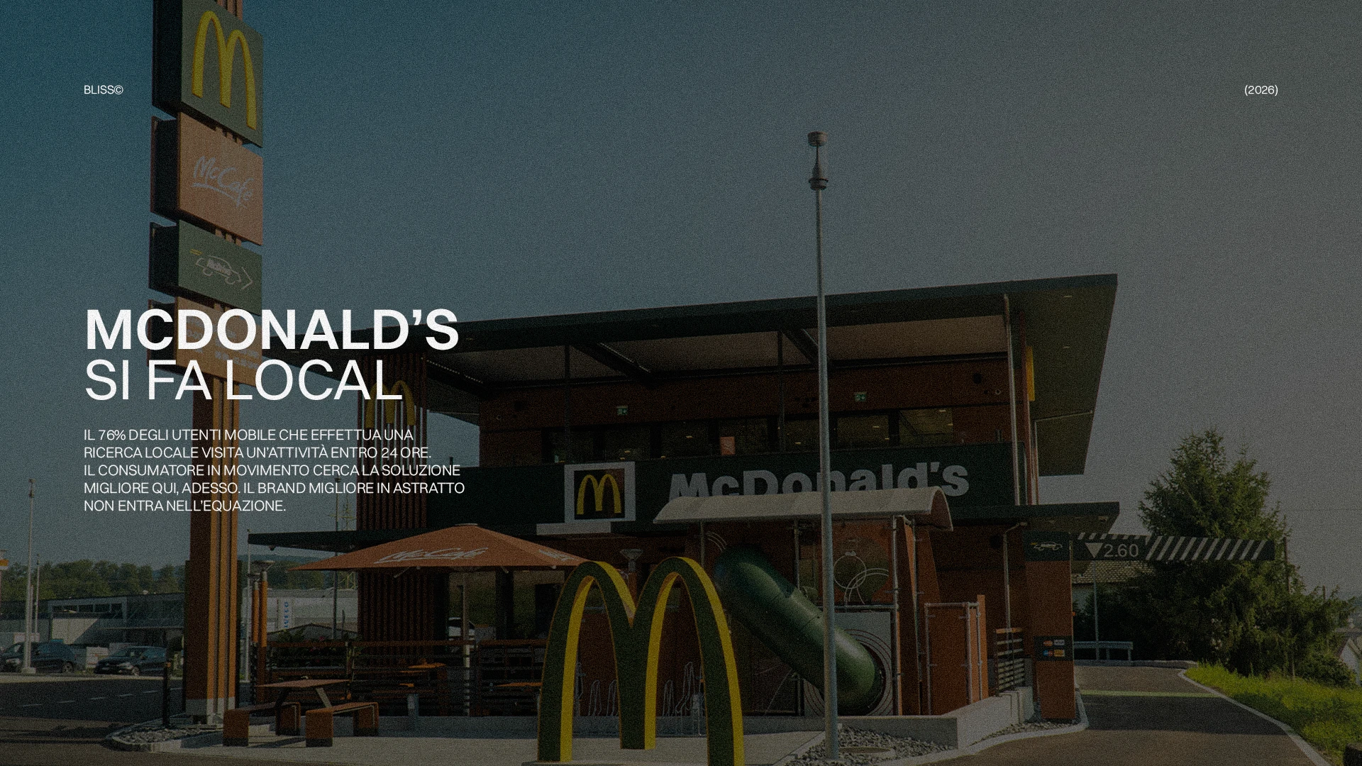 Ristorante McDonald's con testo sovrapposto "MCDONALD'S SI FA LOCAL", insegna alta con loghi multipli e area giochi esterna.